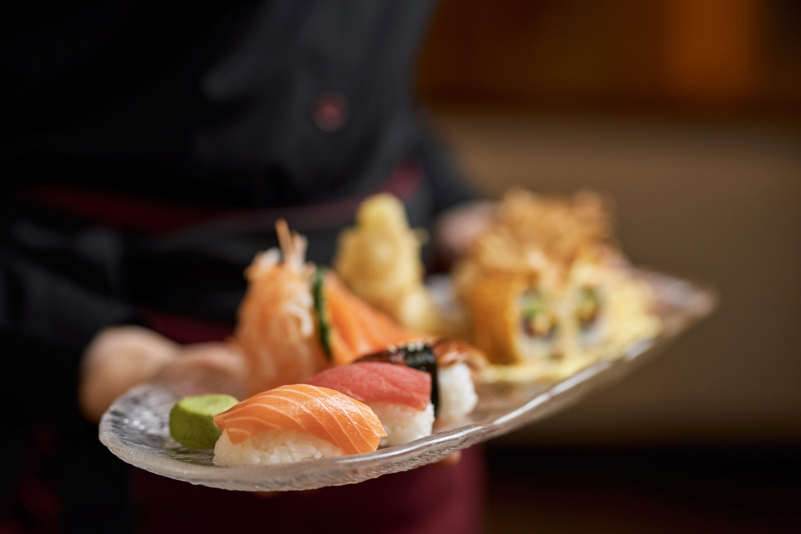 Close-up photo of plate with flavourful sushi and sashimi being carried by a waitress