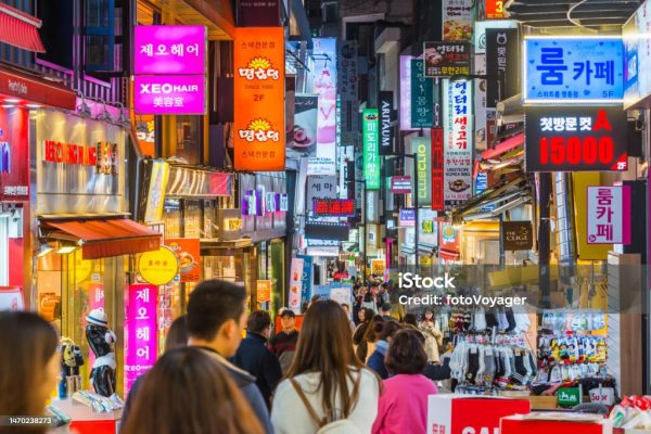 Crowds of shoppers along the pedestrianised streets of Myeong-dong overlooked by the neon lights of stores in the heart of Seoul at night, South Korea’s vibrant capital city.
